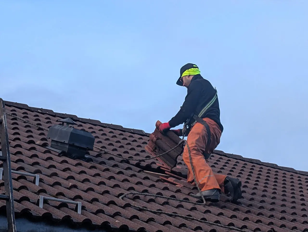 Håndverker på rødt teglsteinstak mot blå himmel
