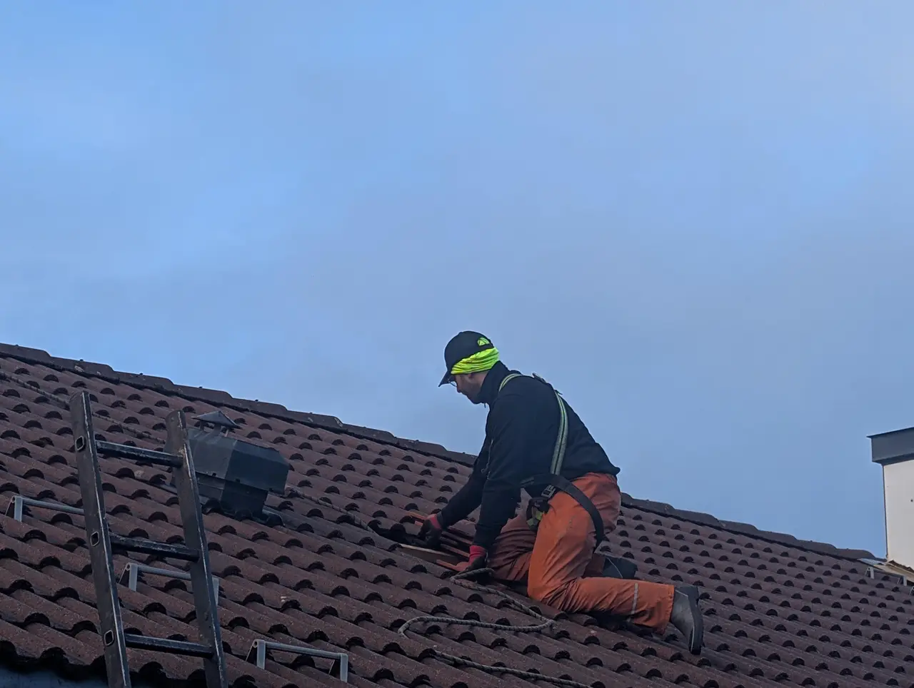 Håndverker i sikringssele sjekker takstein mot blå himmel